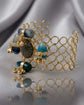 A gold-tone open-link cuff bracelet with turquoise and dark gray cabochon stones, displayed on draped silver satin fabric.